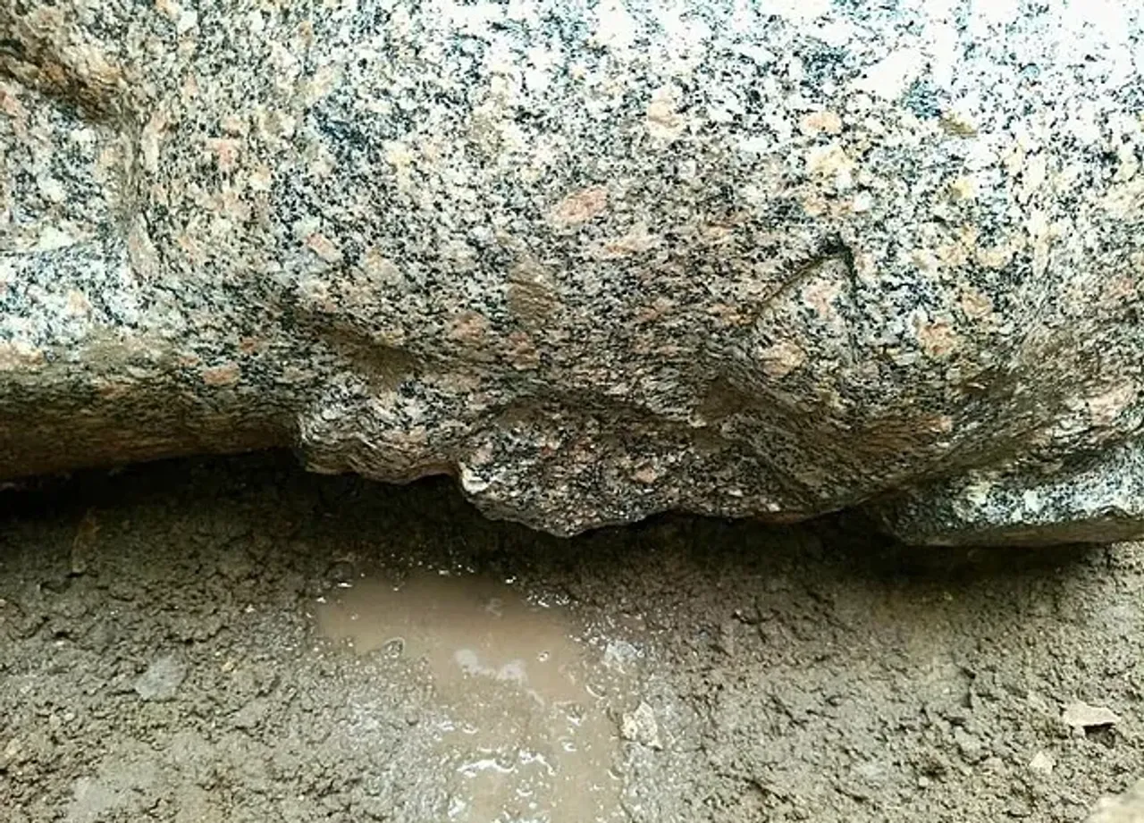 Loyli yer ustida turgan yirik granit toshining yaqindan ko‘rinishi.